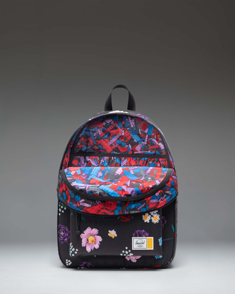 Herschel x LEGO Classic Backpack in the Falling Florals pattern, featuring a black background with colorful LEGO brick flowers and plants.